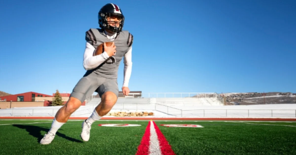 Football player in full gear running on a painted synthetic turf field with clear blue sky.